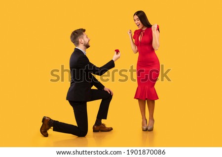 She Said Yes. Man Proposing To Girlfriend Offering Her Ring In Box Standing On Knee Over Yellow Background In Studio Royalty-Free Stock Photo #1901870086