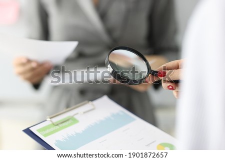 Female hand holds magnifying glass and clipboard with financial figures. Small and medium business development concept