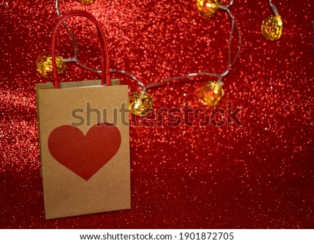 Online holiday shopping, New Year, Valentine's Day, International Women's Day. Shopping or gift bag with heart and lights. Red sparkling background , bokeh effect. Copy space. Selective focus.
