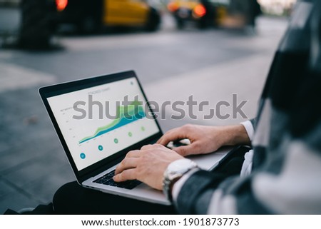 Cropped image of man's hand typing on laptop computer searching information online via 4G internet connection, male student checking graphics and diagrams online on course via technology outdoors