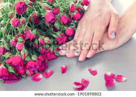 Skin care of a beautiful female hands with art nail manicure. And grey background with small pink roses