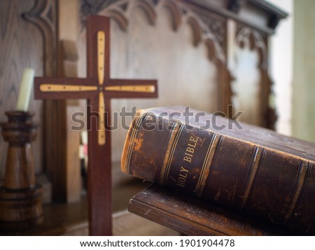 Large holy christian bible closed in old historic Church of England place worship wooden cross in focus sermon prayer from the alter rustic used old book leather bound light reading gods word