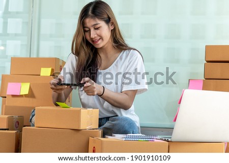 The Asian owner takes pictures of a brown package to verify his customer's address and make arrangements for delivery online while he works at home.