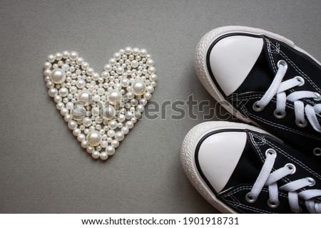 Sports shoes and pearl necklace in the shape of a heart on a paper gray. Valentines day flat lay banner. Chucks and pearls female concept. 