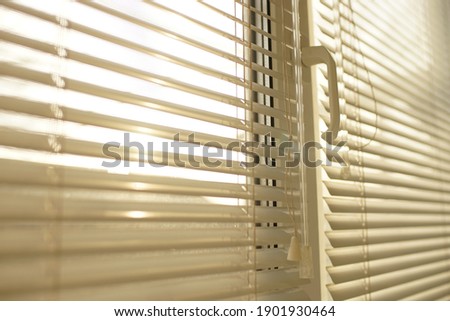 The sun shines through the white horizontal blinds