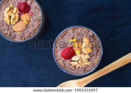 Two glasses of chocolate, orange and chia seed pudding with nut and raspberry topping. Top view, dark blue background.