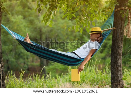 Man with book resting in comfortable hammock at green garden Royalty-Free Stock Photo #1901932861
