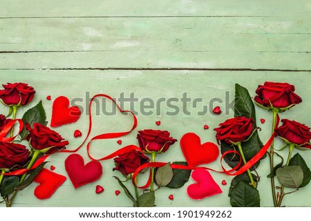 Valentines Day background with assorted hearts, fresh burgundy roses and red festive ribbon. Old wooden gentle green background, flat lay, top view