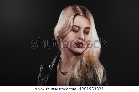 A beautiful, glamour young blond Girl in a black jacket is posing on black background