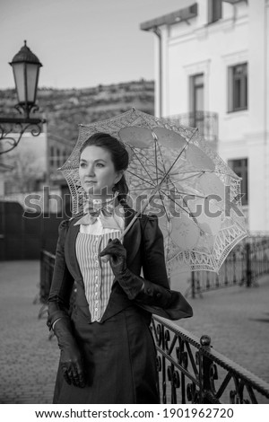 Romantic young beautiful lady walking outdoors with open umbrella. Victorian style vintage. Steam punk concept. White and black photo.