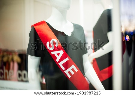 Close up red Sale Sign on mannequin In A Clothing Store. View through a glass of window case. Big discounts because of the store closing. Selective focus. Copy space