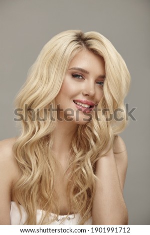 Vertical shot of pretty smiling woman portrait with curly blonde hair and clean skin, studio beauty picture on beige background