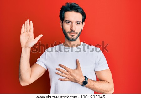 Young hispanic man wearing casual white tshirt swearing with hand on chest and open palm, making a loyalty promise oath  Royalty-Free Stock Photo #1901995045