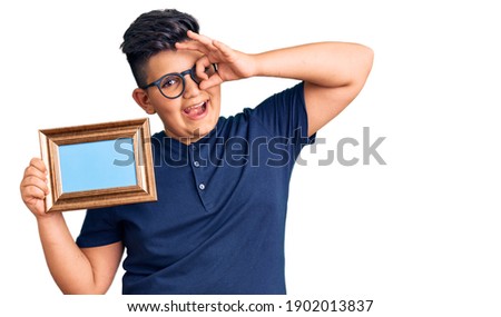 Little boy kid holding empty frame smiling happy doing ok sign with hand on eye looking through fingers 