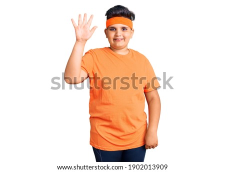 Little boy kid wearing sportswear showing and pointing up with fingers number five while smiling confident and happy. 
