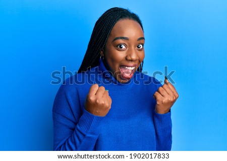 Young african american woman wearing casual winter sweater celebrating surprised and amazed for success with arms raised and open eyes. winner concept. 