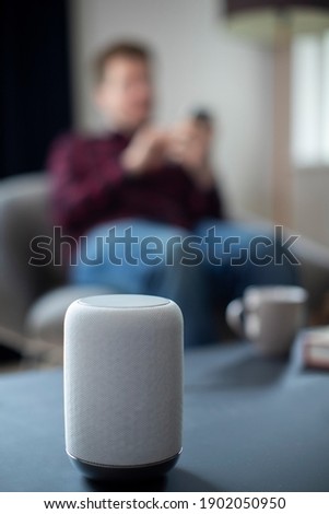 Man Streaming Music Or Podcast To Smart Speaker From Mobile Phone At Home