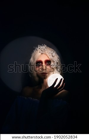a fabulous, magical photo as a cover for a book, a novel. A beautiful woman with dark makeup of a sorceress or priestess holds the moon on a black background in a beam of light