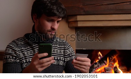 Man shopping online using smartphone at home sitting by the fireplace