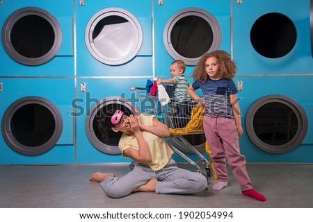 Mother Household With Children Wearing Pyjamas Having Fun And Doing Laundry At Self Service Laundrette Near Washing Machines. Housework Together