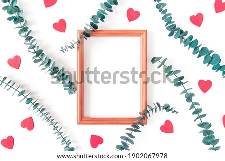 Eucalyptus branches, red wooden figurines in the shape of a heart and an empty wooden photo frame are on a white background. Composition for Valentine's Day. Flat lay. Top view. Copy space.