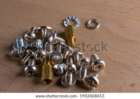 A set of small, nickel-plated computer screws scattered on a wooden table