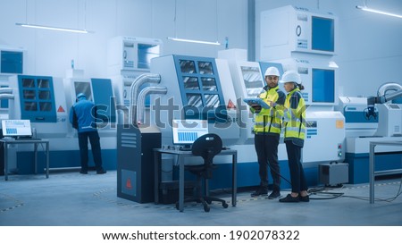 Chief Engineer and Project Manager Wearing Safety Vests and Hard Hats, Use Digital Tablet Controller in Factory, Optimizing CNC Machinery Programming Machine for Increasing Production Line Efficiency Royalty-Free Stock Photo #1902078322