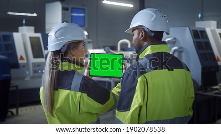 Industry 4.0 Factory: Chief Engineer and Project Supervisor in Safety Vests and Hard Hats, Talk, Use Digital Tablet Computer with Green Screen, Chroma Key. Workshop with Machinery.