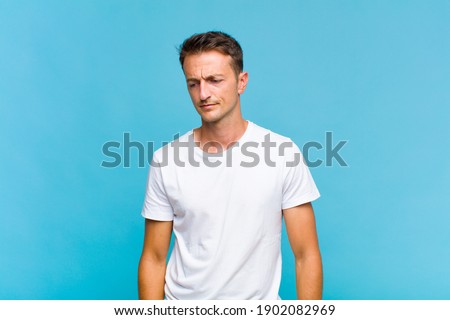 young handsome man feeling sad, upset or angry and looking to the side with a negative attitude, frowning in disagreement