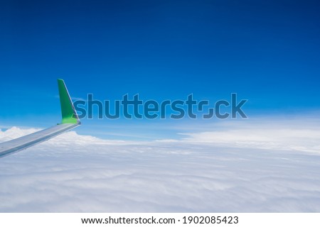 The wing tips of the airplane against white fluffy cloud and clear blue sky background while travelling in the summer.