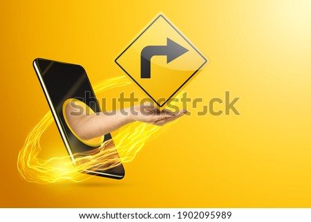 The hand crawling out through the smartphone shows a yellow road sign with a black arrow, yellow background. Navigator concept, gps navigation, location app. Copy space