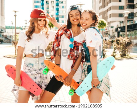 Three young smiling beautiful female with colorful penny skateboards. Women in summer hipster clothes posing in the street background. Positive models having fun and going crazy
