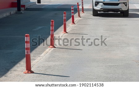 Row of orange plastic traffic posts with blurred motion front view of white car slow running into outdoor parking lot area