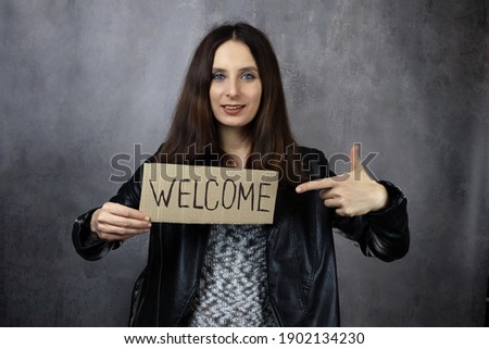 woman holds a piece of paper with the word Welcome in her hand on a gray background