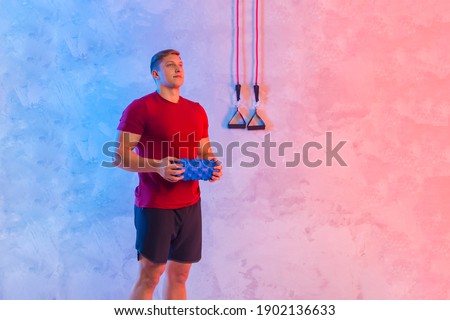 Athletic trainer with blue massager and rubber resistance bands teaches group fitness and work out online training on a bright neon background. Sport online concept
