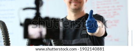 Happy male worker in special clothes repairing a bicycle and shooting video content