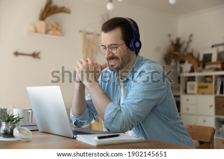 Personal achievement. Happy young man sit before pc screen in headphone set listen to prof tutor teacher at online conference. Male student feeling glad proud getting high grade doing task successful Royalty-Free Stock Photo #1902145651
