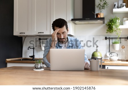Any idea. Thoughtful young man freelancer spending time at home by kitchen table using laptop pc thinking on difficult problem. Pensive remote student is unsure having doubts in finding correct answer