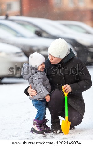 Mother quieten her crying toddler child on snowy street, hugging and kissing a son
