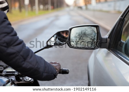 Motorcycle rider touching side mirror of a car when riding nearby on a road, close-up view Royalty-Free Stock Photo #1902149116