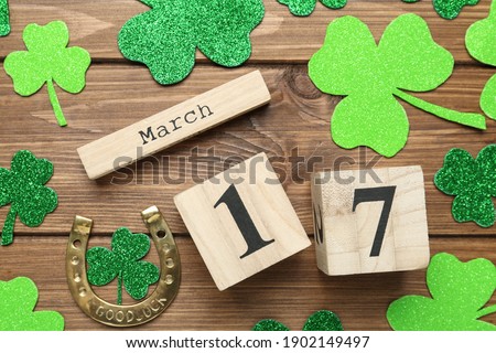 Decorative clover leaves, horseshoe and block calendar on wooden background, flat lay. St. Patrick's Day celebration