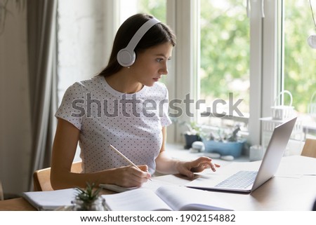 Taking exam online. Worried young woman pass examination from home at quarantine via virtual education platform. Nervous female student answer questions of control test review work using pc headphones Royalty-Free Stock Photo #1902154882