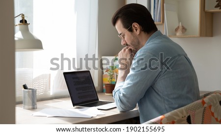 Thinking on text. Thoughtful young man working on document online or pondering on translation of electronic book in foreign language. Concentrated focused male author creating story using laptop app