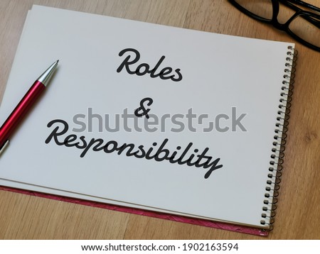 Text Roles and Responsibility on note book with pen and eye glasses on wooden table.