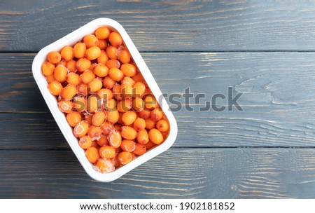 Frozen sea buckthorn berries in a container on a wooden background with place for text. The concept of preparing food for the winter.