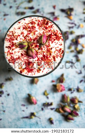 Close up of a cup of fresh cappuccino with pink and red flowers on light blue background