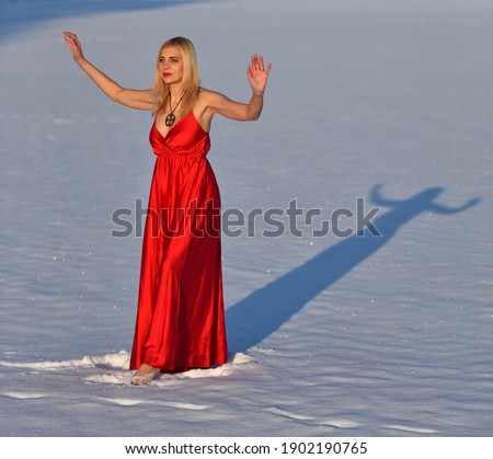 Woman in long open red dress on the snow in winter. Contrast concept. Full height portrait. Red lips. Sparkling snow. Mindfulness, natural, piece, relax, harmony, balance, vitality, energy concept. 