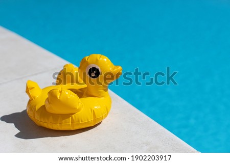 Inflatable yellow mini duck, cocktail stand near swimming pool on bright sunny day, copy space. Concept of summer vacation, entertainment, water, air, sunbathing, health. Side view. Horizontal.