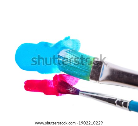 two brushes wide and narrow make strokes of dark red and blue paints on a white background. copy space.