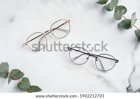 Women's glasses and eucalyptus leaves on marble table top view.  Royalty-Free Stock Photo #1902212701